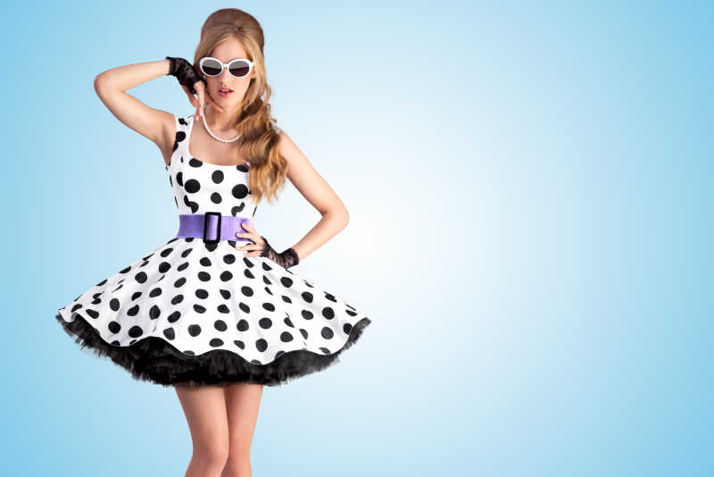 蓝色背景身着复古圆点礼服和太阳镜的金发女孩