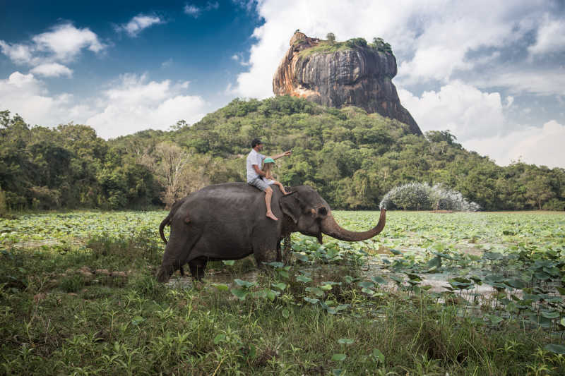 岩石为背景骑在大象背上的男子和儿童