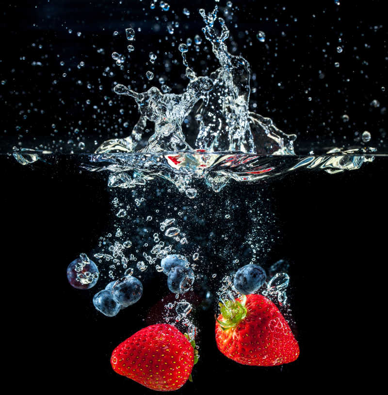 黑色背景下溅入水中的草莓和蓝莓镜头