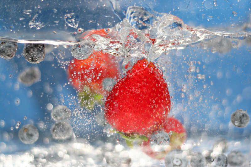 多汁的红草莓和蓝莓掉入波光粼粼的水中特写