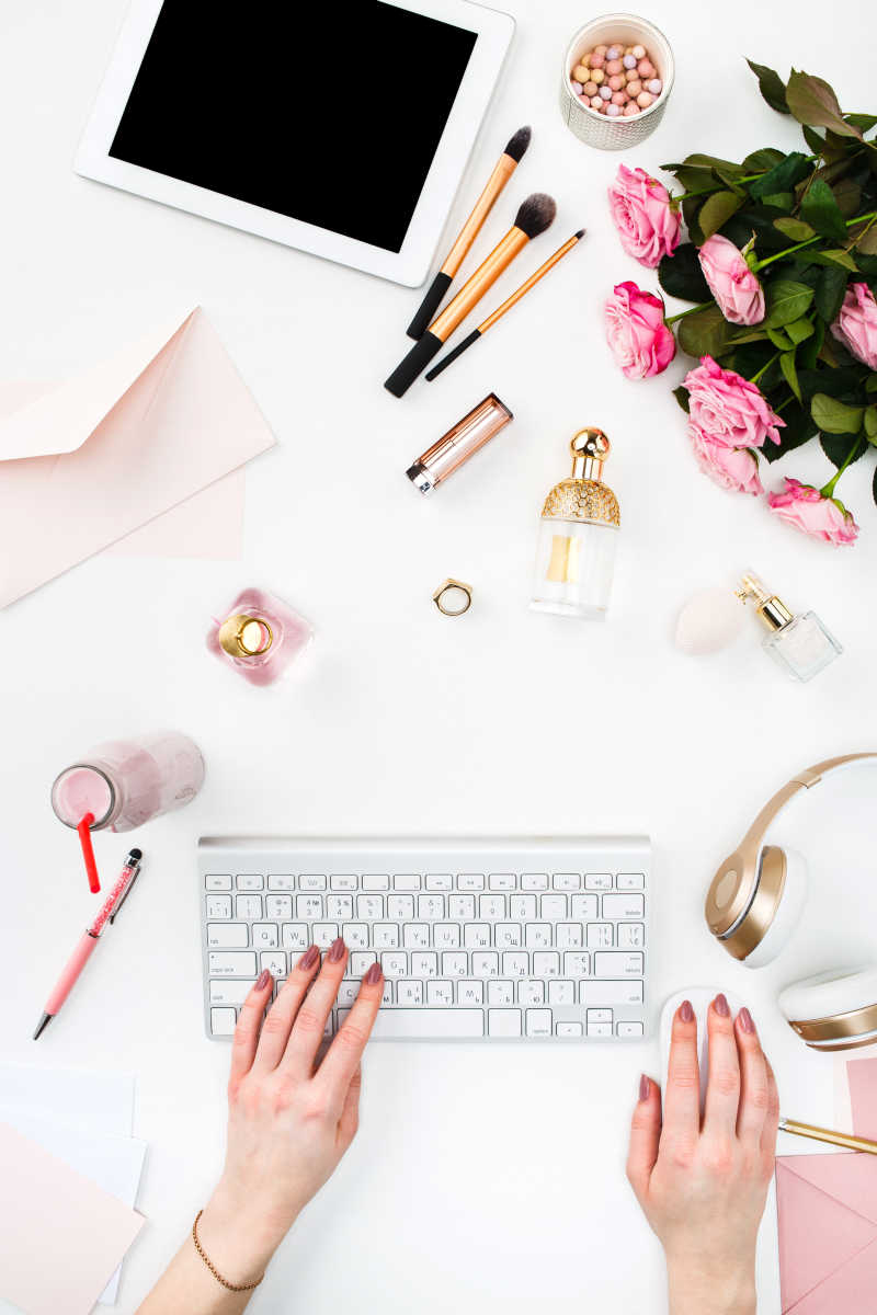 键盘上的女性手和旁边的日常化妆品