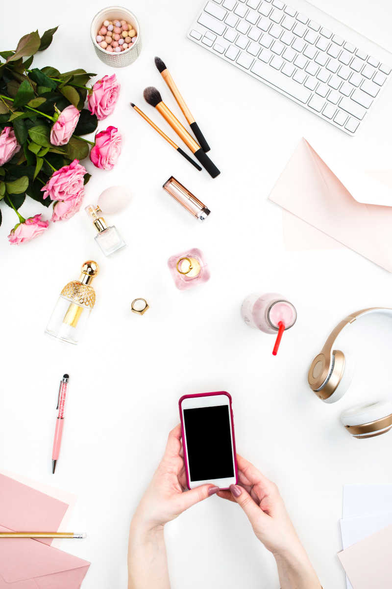 女性手拿智能手机和旁边的日常配件用品