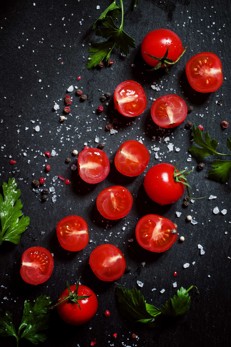 黑色背景上的切开的番茄和香料