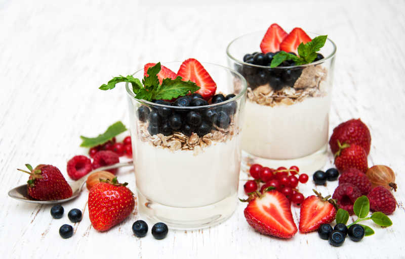两杯酸奶上放着新鲜蓝莓和草莓