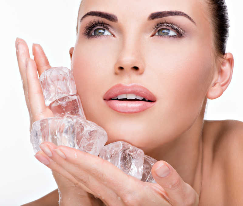 美丽的年轻的女子把冰敷在脸上
