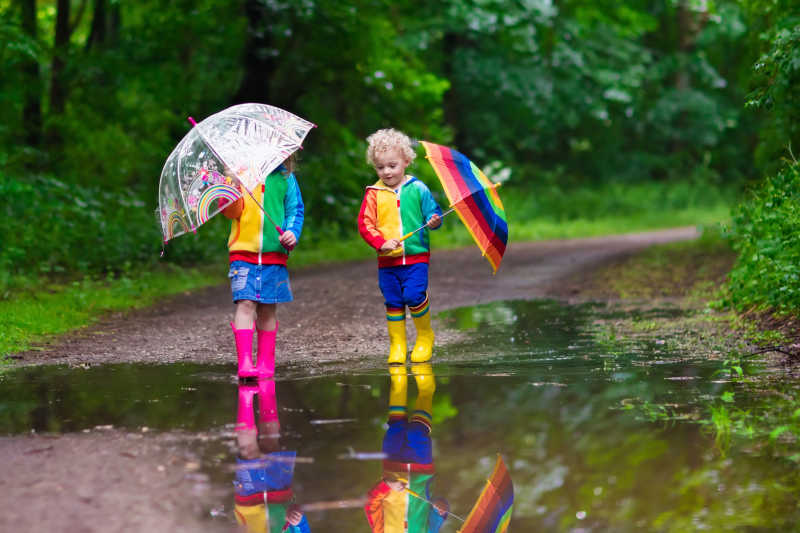 小男孩和女孩在多雨的夏季公园里玩耍