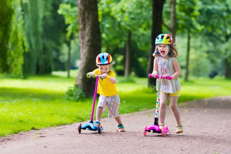 阳光明媚的夏日孩子们在公园里学骑滑板车