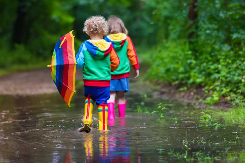 小男孩和女孩走在多雨的夏季公园小路上