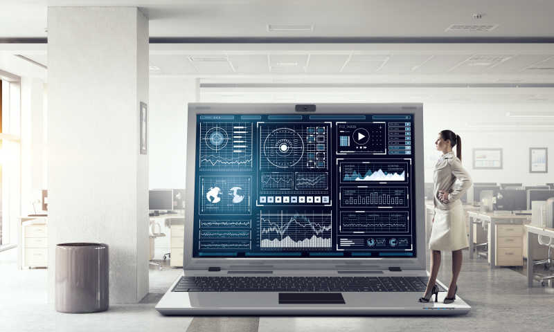 叉腰站在大笔记本电脑的图形和图表的年轻商人