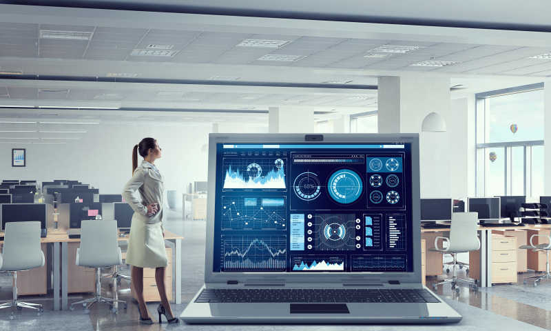 叉腰站在现代室内大笔记本电脑的图形和图表的年轻女人