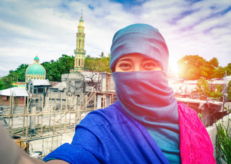 年轻女孩在日落与清真寺和尖塔的背景下拍写真