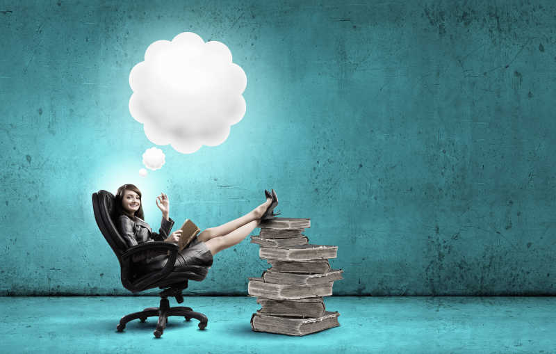 年轻的女人坐在椅子上手里拿着一本书