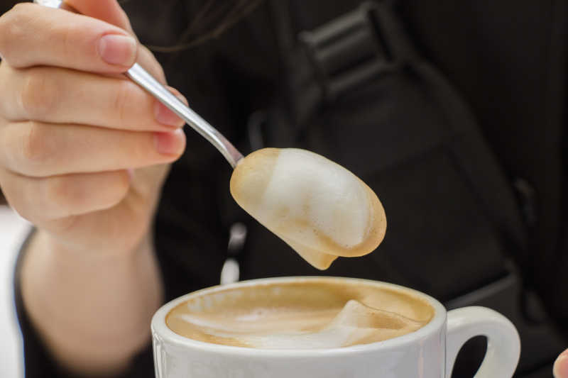 手拿杯勺和卡布奇诺