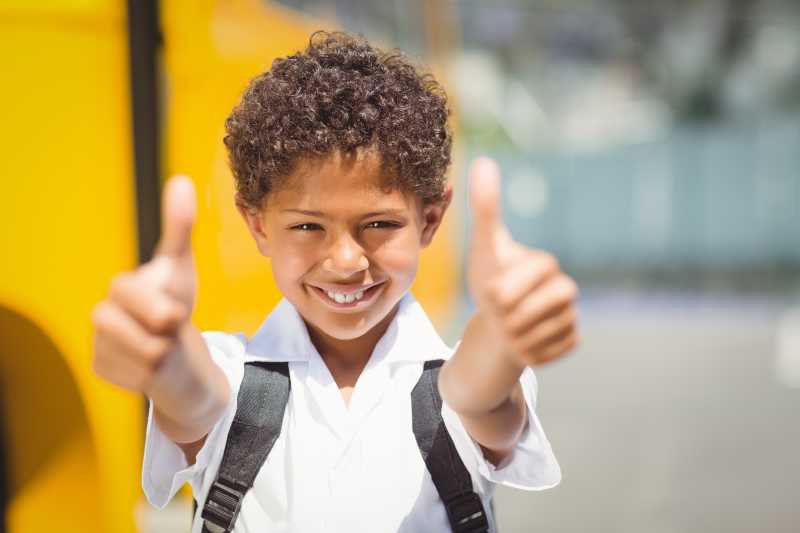 可爱的小学生在校车旁对着摄像机微笑