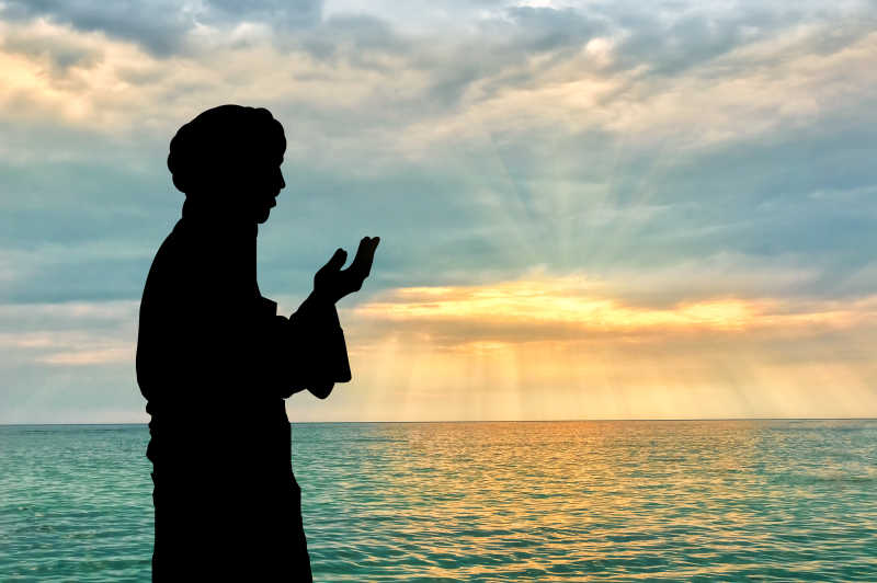 在海边和美丽的落日下祈祷的男人