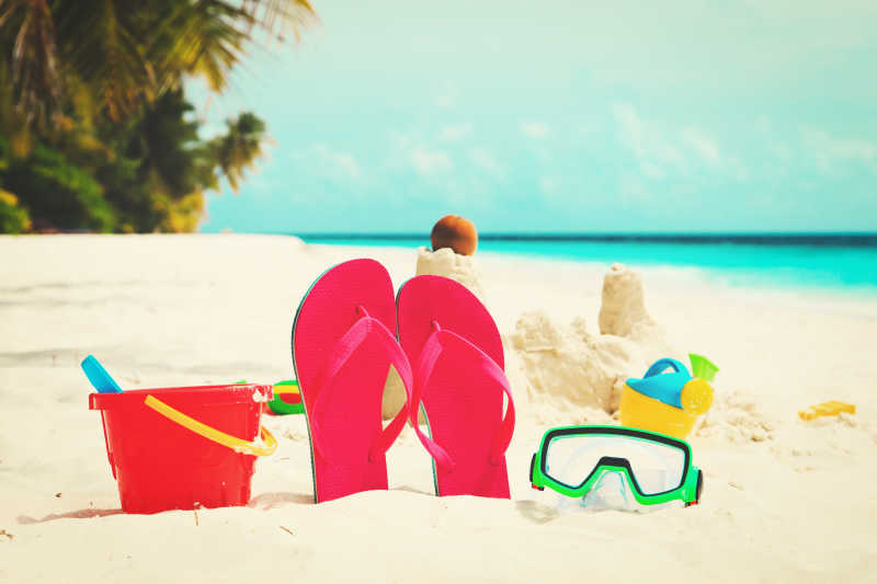 各种玩具和一双立在沙滩上的红色拖鞋