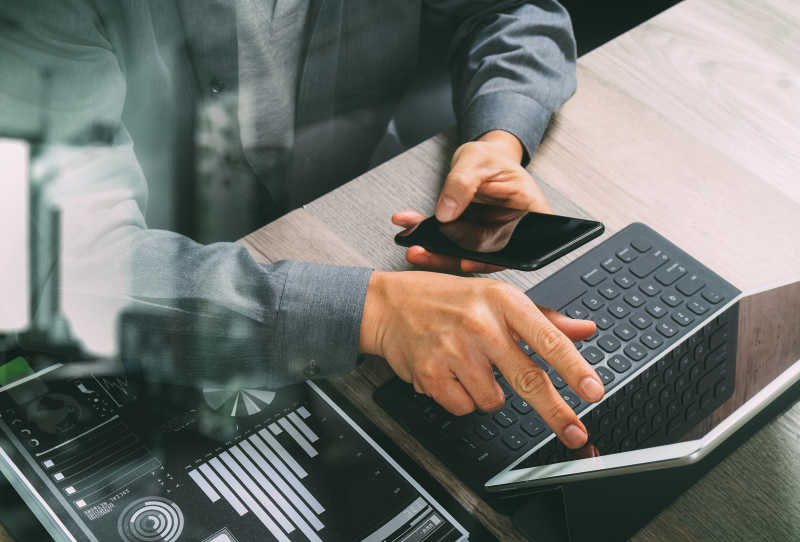 坐在凳子上的商人在使用智能手机与平板电脑