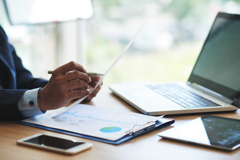 坐在电脑前拿着文件在看的男人