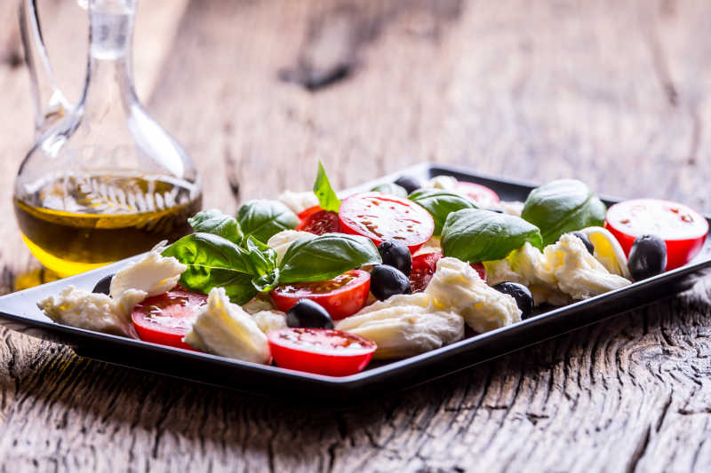 木桌上美味的卡普雷塞沙拉和橄榄油特写