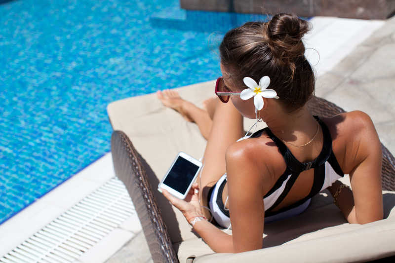 年轻女子拿着手机与耳机靠在日光沙发上