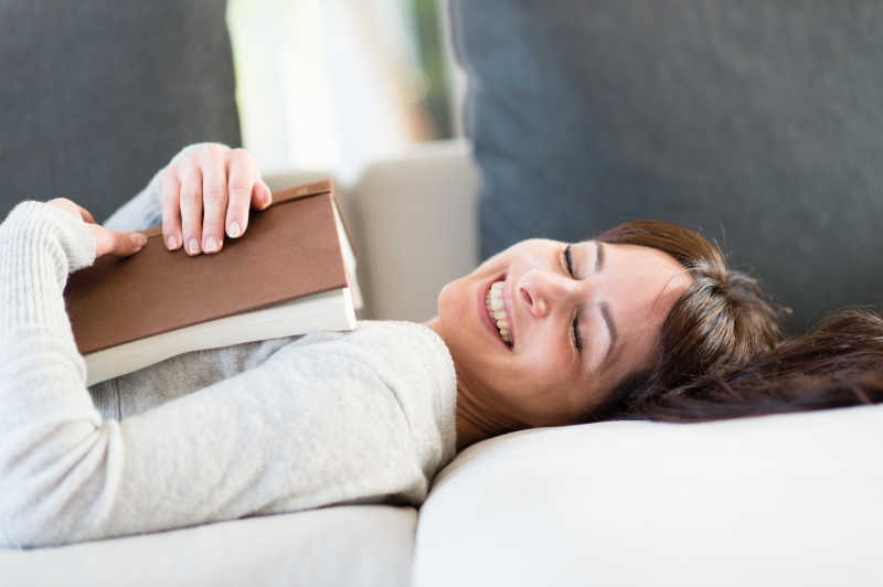 居家年轻女子抱着书本畅想着