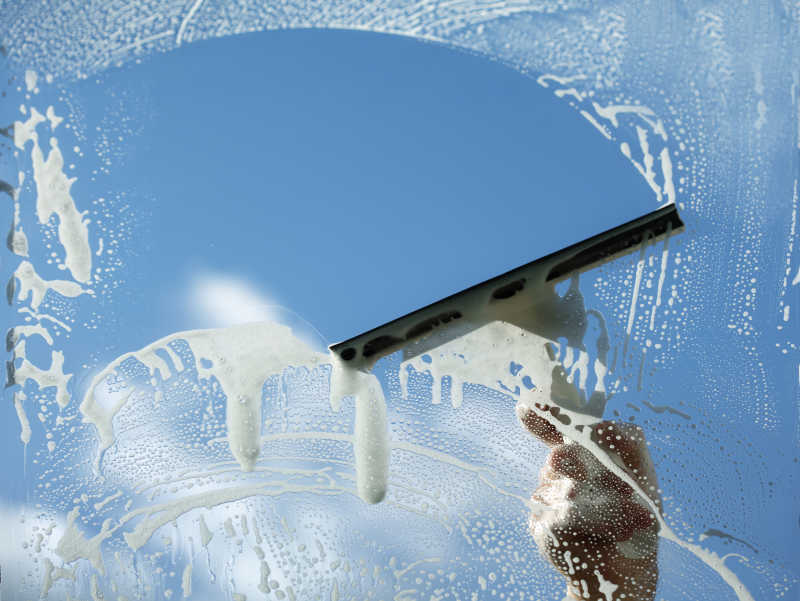 蔚蓝的天空下用刮刀洗窗器清洁玻璃