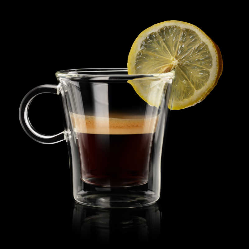 黑色背景下装有浓咖啡和柠檬片的透明杯