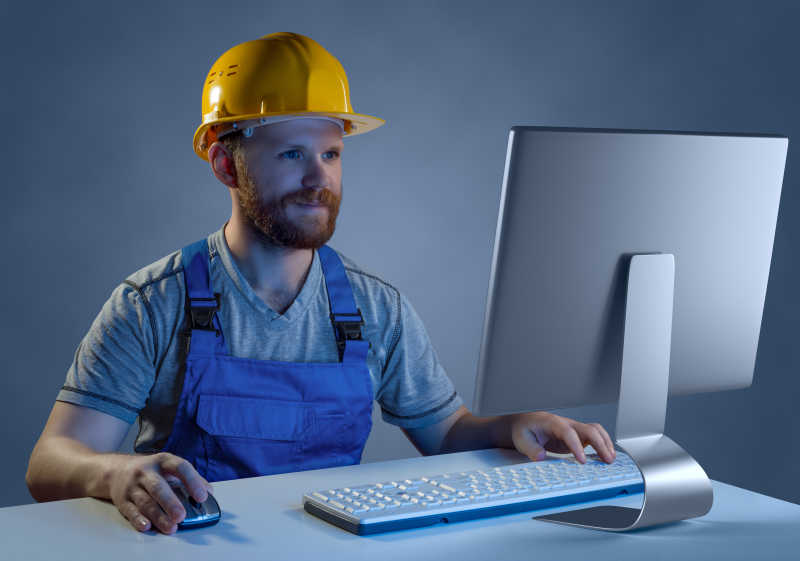 工人建设者在头盔和统一在计算机上工作