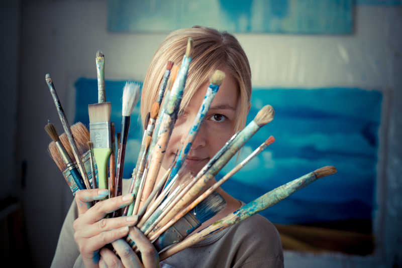 拿着许多画笔的金发美女画家