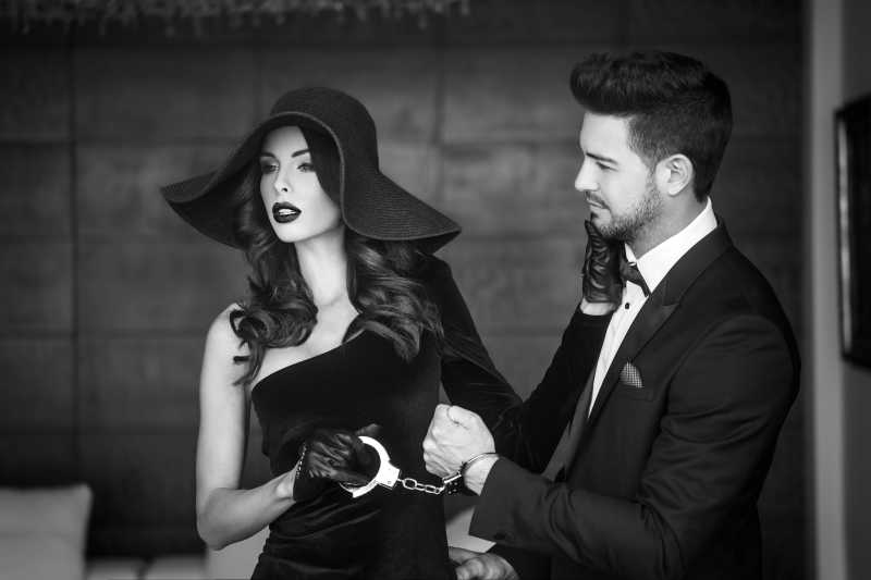 戴帽子的女人拿着手铐和铐着手铐的男人