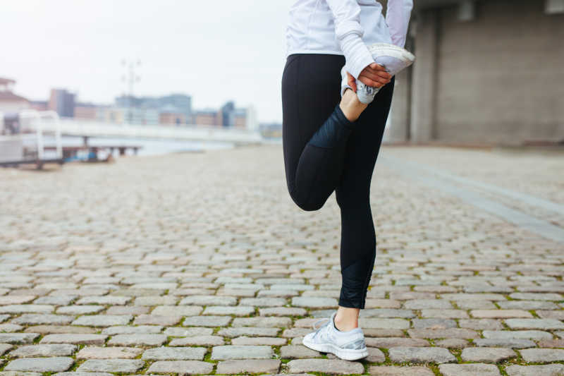 年轻女子在城市街道做跑步前伸展腿部运动