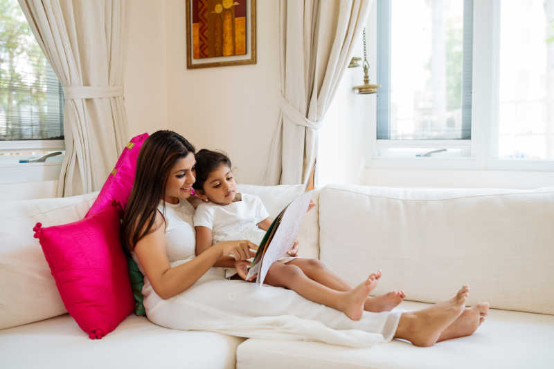 沙发上的妈妈正在给女儿读书特写