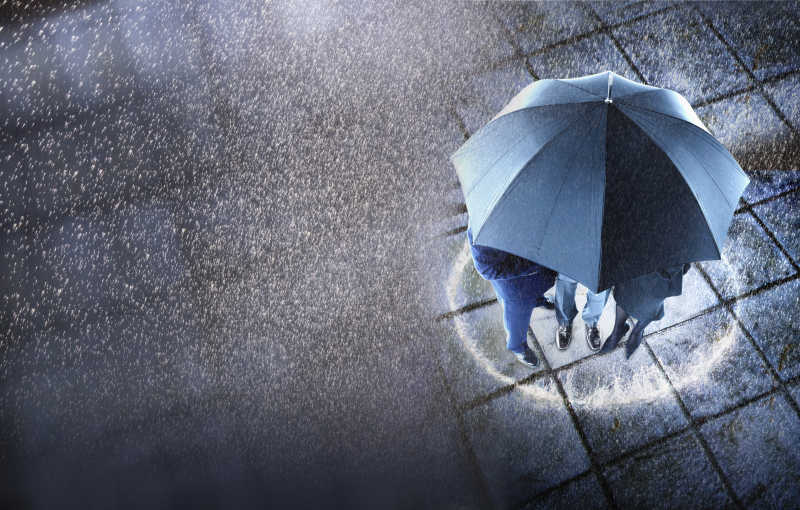 下雨的天气里三位商人围在一把雨伞躲雨