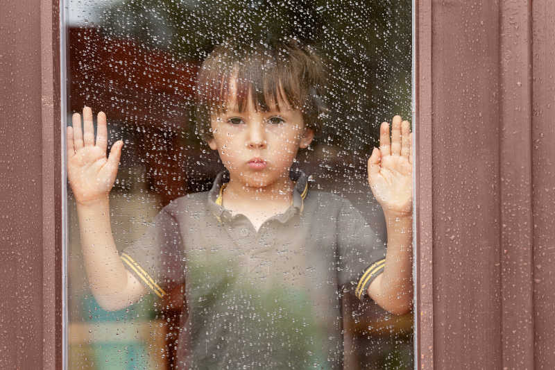 小男孩透过窗户看着外面的下雨天