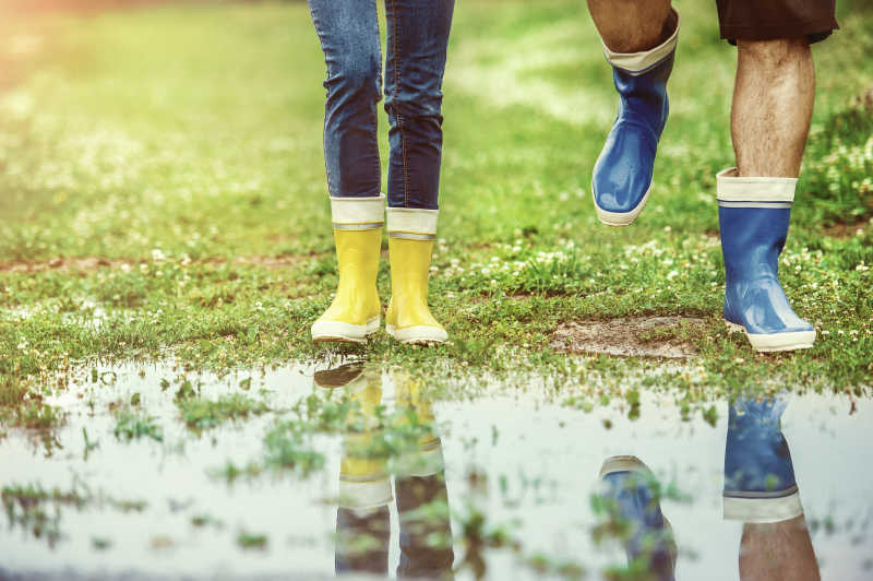 草地水坑旁穿雨靴的男女脚部特写