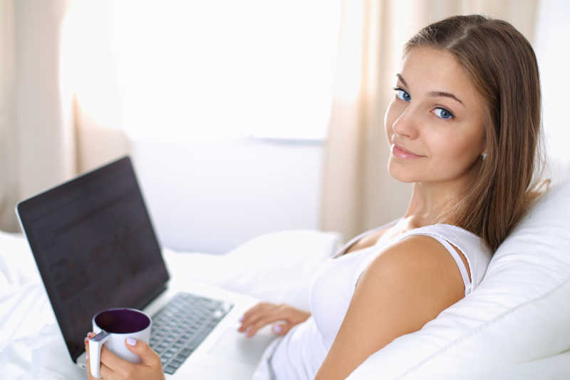 年轻美女躺在床上用笔记本电脑办公