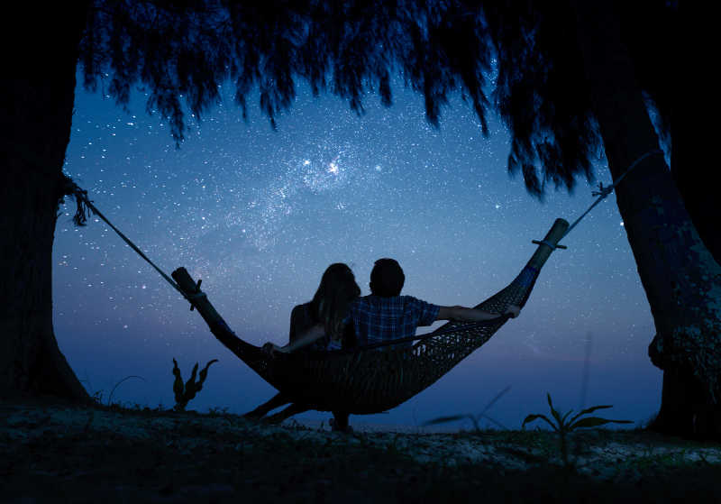 坐在吊床上的情侣看着美丽的夜空
