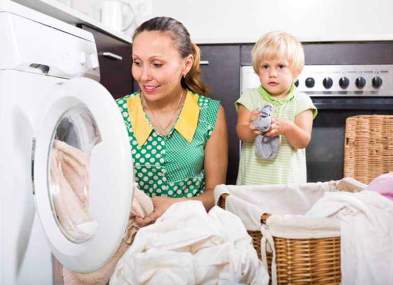 用洗衣机洗衣服的戴着女儿的家庭主妇