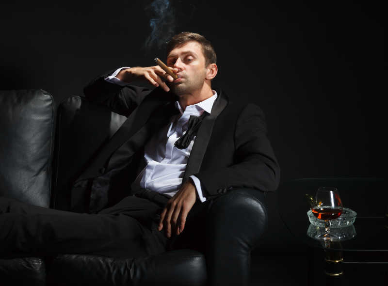 坐在黑色沙发上的抽雪茄的男士