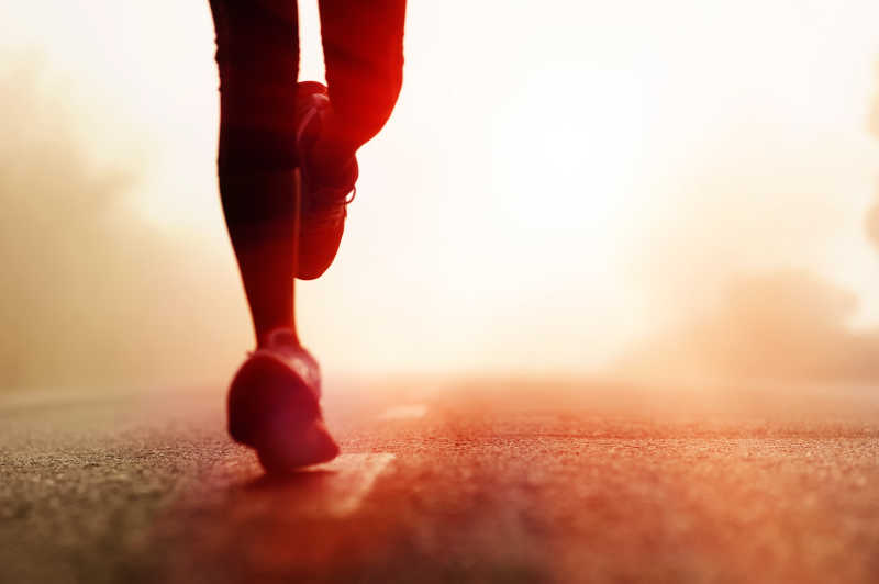昏暗的阳光下在公路上跑步运动员的脚部特写