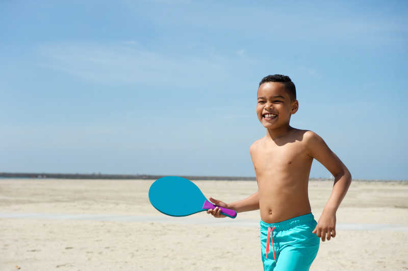 小男孩在沙滩上玩桨球