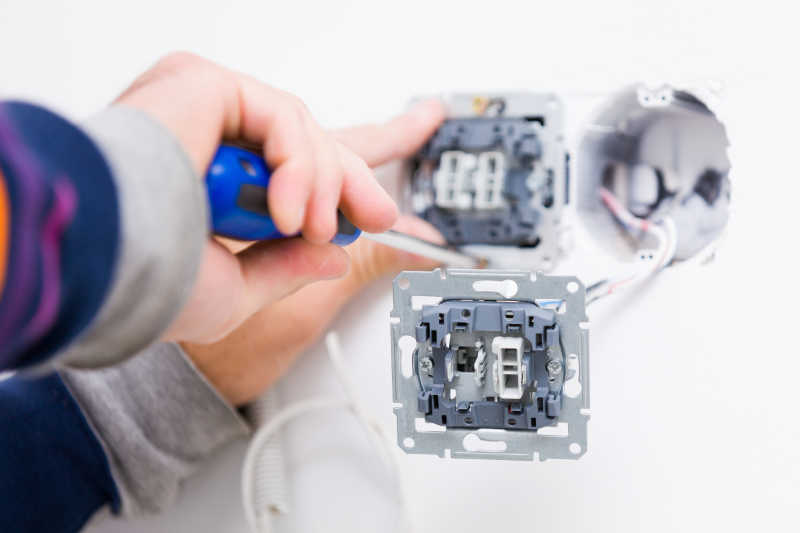 电工拿着螺丝刀在白色的墙上安装插座