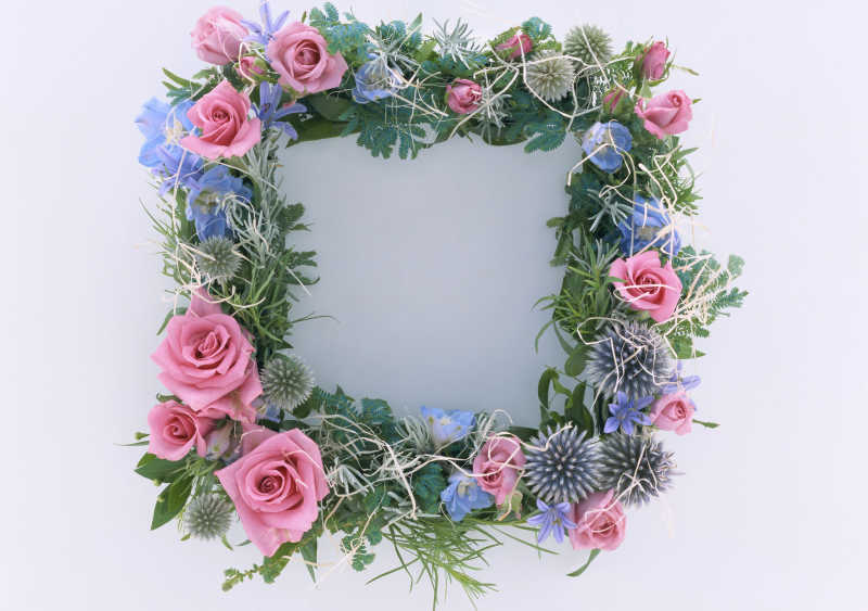 白色背景下粉色的花和绿色的叶子编织成的花环