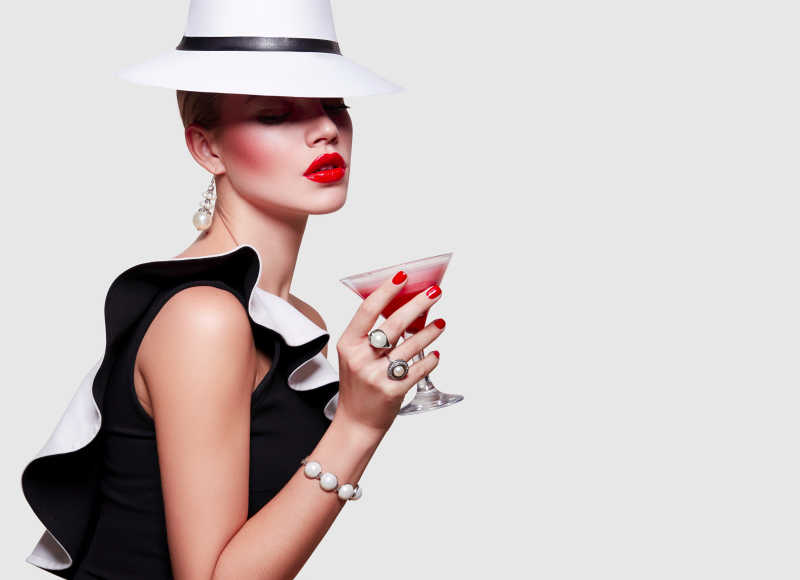 白色背景下着黑白装束的美丽女孩端着红色的鸡尾酒