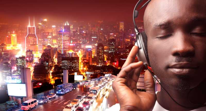 在繁华街道背景下的黑人小伙带着耳机享受音乐