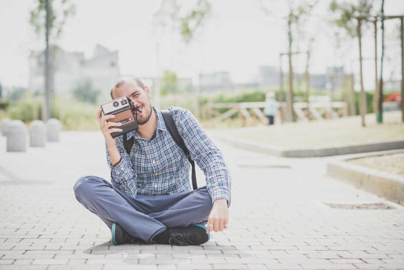 坐在街道上拿着相机拍摄的微笑摄影师