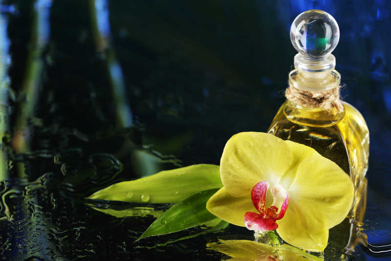 黑暗的彩色背景下的兰花与水滴和香水瓶