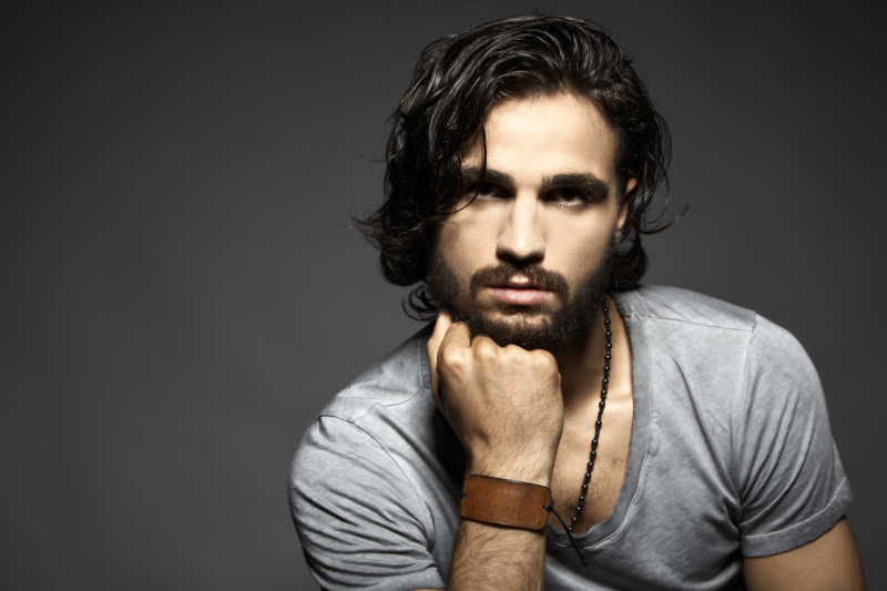 灰色背景下用手拄着下巴的英俊青年男子肖像