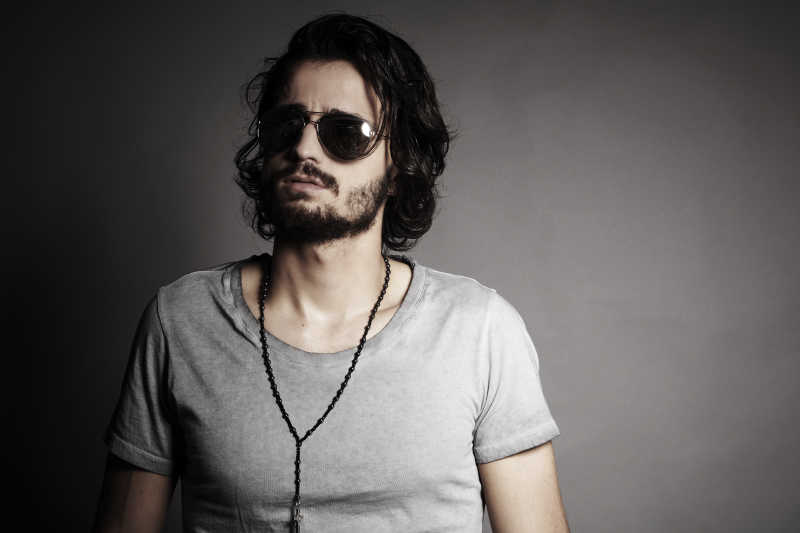 灰色背景下带着墨镜的时尚男子肖像