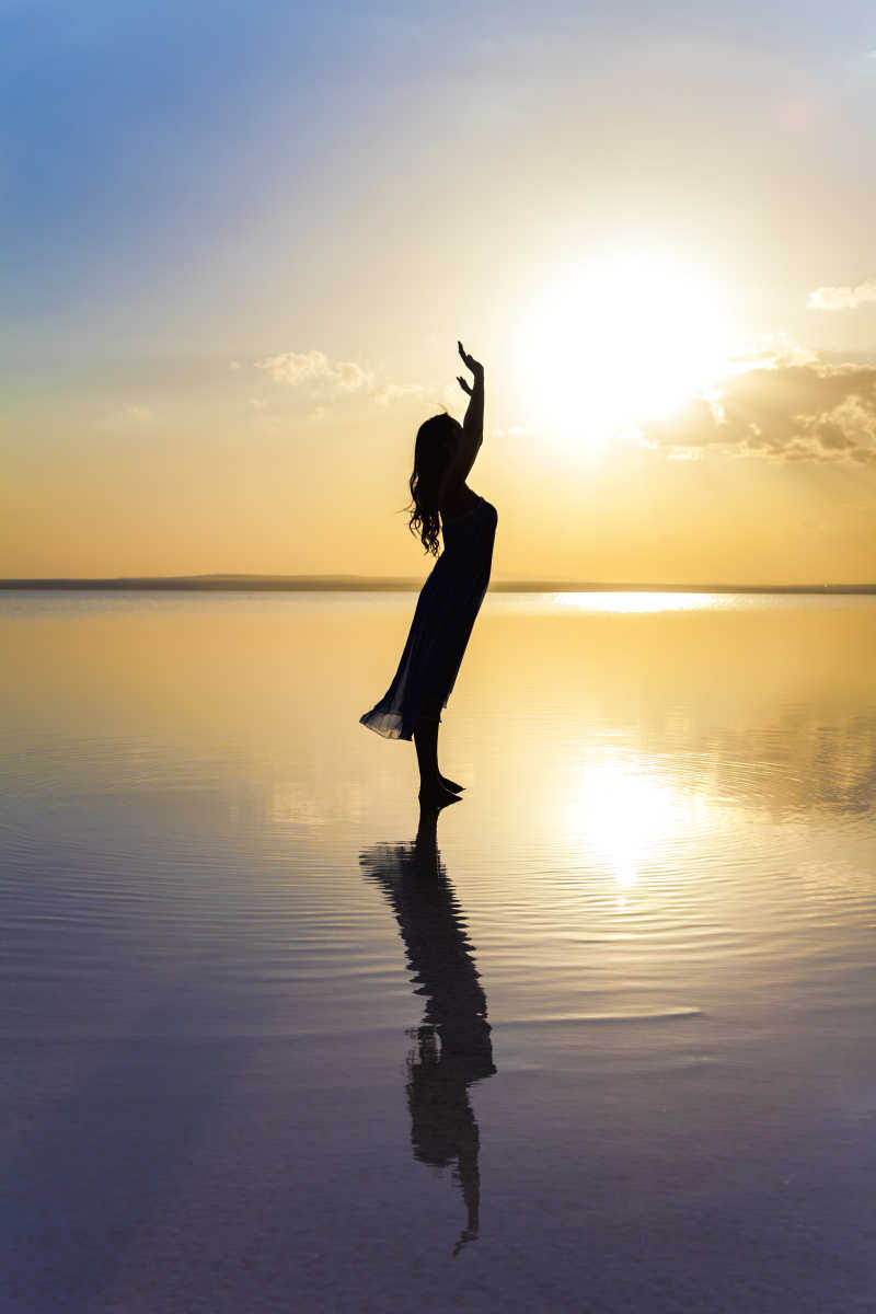 夕阳下站在水面上举着双臂的女人